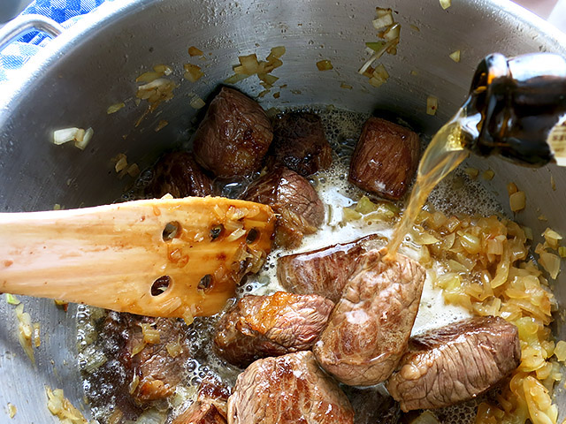 Biergulasch Bier angießen auf Fleisch und Zwiebeln